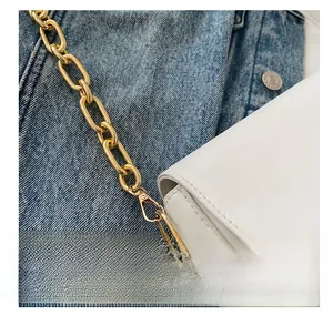 Close-up of white crossbody bag featuring a textured finish and gold metal chain link