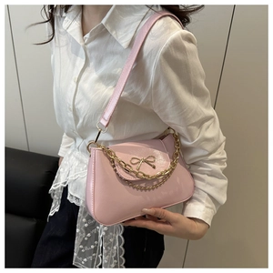 Pink underarm bag detail featuring a gold bow accent and elegant layered chain straps