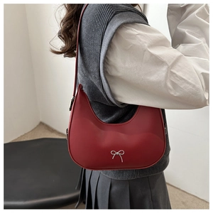 Detail of red crescent shoulder bag with silver bow accent on model in preppy style