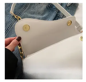 Close-up of the gold magnetic buckle and fine stitching on a white saddle bag
