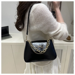 Detail of black leather shoulder bag featuring a gold bow clasp and decorative chain