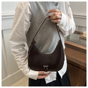 Close-up of a coffee brown crescent bag featuring a silver bow accent on a model