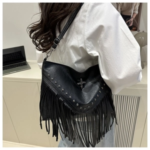 Detail of black leather crossbody bag with long tassels, silver studs and cross hardware