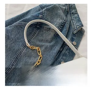Detail of white leather shoulder bag featuring bold gold chain strap on denim fabric