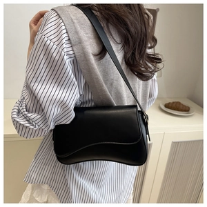 Side view of black minimalist saddle bag with wave-shaped flap worn on the shoulder