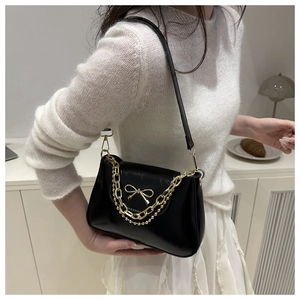 Close-up of black glossy underarm bag featuring a golden bow and textured metal chain