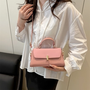 Minimalist pink leather handbag with gold buckle and top handle shown on a model