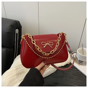 Detailed macro view of red glossy patent leather shoulder bag with gold bow clasp