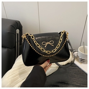 Detailed shot of a black glossy shoulder bag featuring a gold bow and metallic chains
