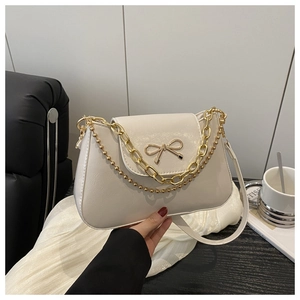 Close-up of ivory shoulder bag with golden bow hardware and chunky chain detail