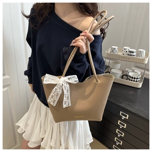 Detalle de bolso tote de cuero caqui con lazo de encaje blanco y letras doradas finas