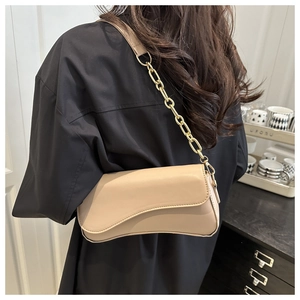 Detail of beige asymmetric flap bag with gold chain strap worn by a model