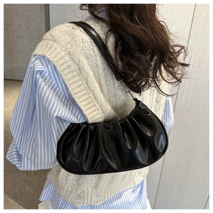 Gros plan sur un sac croissant plissé noir en cuir mat porté à l'épaule par un mannequin