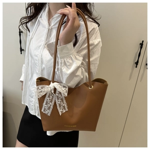 Detalle de bolso tote marrón con lazo de encaje blanco y letras doradas de moda