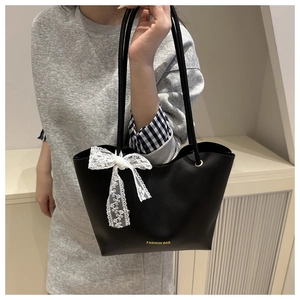 Detalle de bolso tote negro minimalista con lazo de encaje blanco y texto dorado