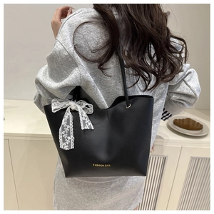 Modell trägt eine schwarze matte Tote-Tasche mit weißer Spitzenschleife und Goldakzent