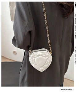 Detail of a white heart-shaped quilted bag with gold chain strap and stitching