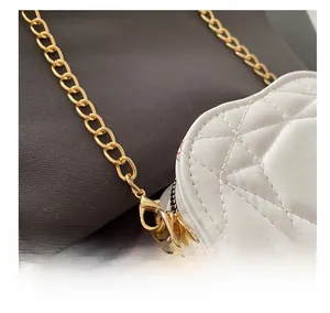 Close-up of golden metal chain hook and quilted leather detail on white heart-shaped bag