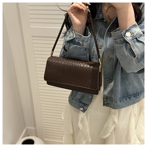 Detailed view of woven texture and metal buckle on dark brown leather baguette bag