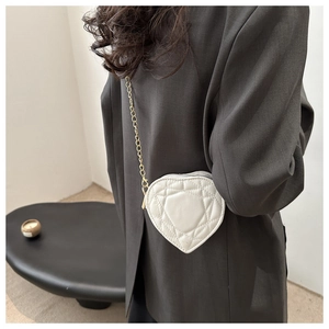 White heart-shaped quilted bag with gold chain strap shown on person's side