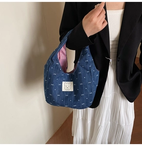 Nahaufnahme einer Denim-Tragetasche mit Schleifenmuster und Bären-Patch am Model