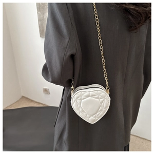 Detail of white heart-shaped quilted bag with gold chain strap on a model shoulder