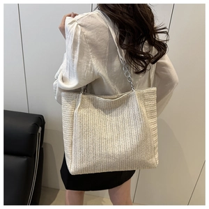 Detail of herringbone woven texture and silver chain strap on beige straw tote bag