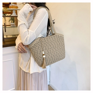 Detail of hand-woven straw tote bag with white beads and wooden tassel charm