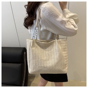 Detail of cream woven tote bag featuring silver chain strap and herringbone weave texture