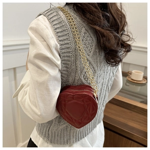 Detail of red heart-shaped quilted bag with gold chain strap on a stylish outfit