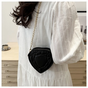 Detail of black heart-shaped quilted leather bag with gold chain and elegant textures