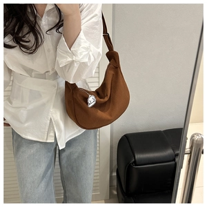Detail of brown corduroy crescent bag featuring a cute white puppy charm and wide strap