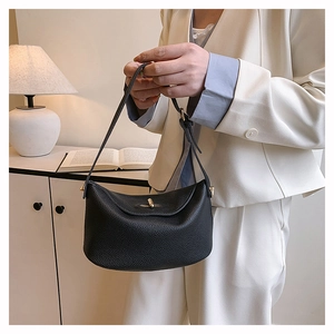 Detail of black pebbled leather bucket bag with gold hardware held by a model