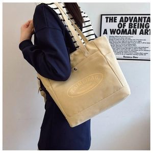 Detail view of beige canvas tote bag with logo and side pocket on model