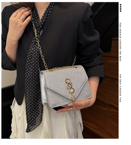 Détail d'un sac bandoulière argenté pailleté avec boucle dorée en S et chaîne en métal