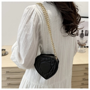 Model wearing black heart-shaped quilted shoulder bag with golden chain strap on white dress