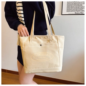 Detail of canvas tote bag with side pockets and magnetic closure shown on a shoulder