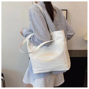 Detail of white canvas tote bag showing side pocket and yellow TAIMEIBAG logo print