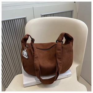 Détail d'un sac bandoulière marron texturé gaufre avec un charm chien blanc sur une chaise