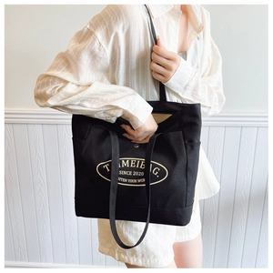 Minimalist black canvas tote bag with oval logo shown on a person for casual style