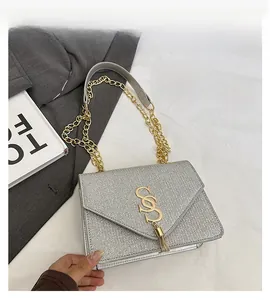Detail of silver textured flap bag with golden S-logo, tassel and metal chain strap