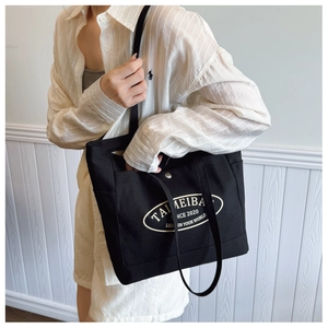 Detail of black canvas tote bag showing side pocket and white printed logo design