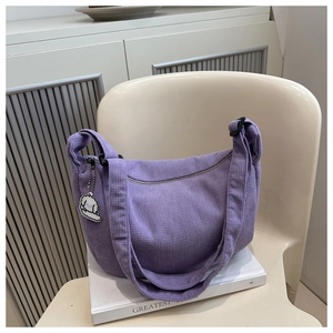 Détail du sac croissant en velours côtelé violet avec breloque mouton blanc sur chaise crème