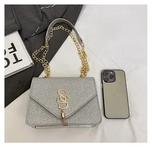 Detail of silver glitter crossbody bag with gold logo, tassel, and chain strap for scale