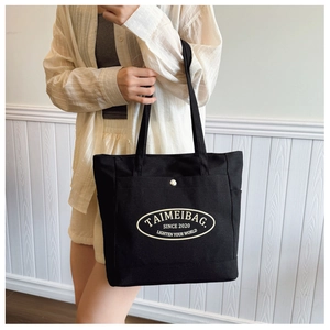 Close-up of black canvas tote bag with white minimalist logo print and double straps