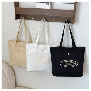 Detail of canvas tote bags in cream, white, and black with oval logo and metal fastener