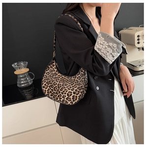 Leopard print crescent shoulder bag shown on model in a stylish cafe setting