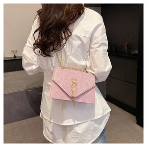 Modèle portant un sac bandoulière rose pailleté avec chaîne dorée et pompon 'S'