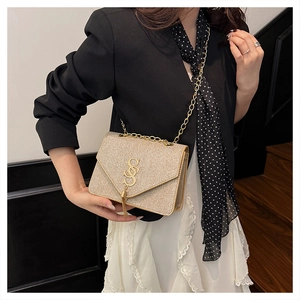Close-up of gold sequined shoulder bag with metallic logo tassel and chain strap