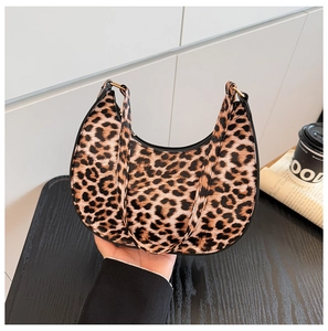 Close-up of leopard print crescent bag with black piping and gold rings on a cafe table